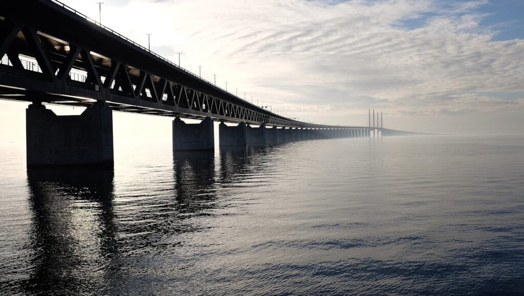 Grey Concrete Bridge on Body of Water Under Blue and White Sky during Daytime